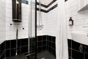 Ein modernes Badezimmer mit schwarz-weißer Fliesenoptik, einer Duschkabine aus Glas und einem weißen Waschbecken.