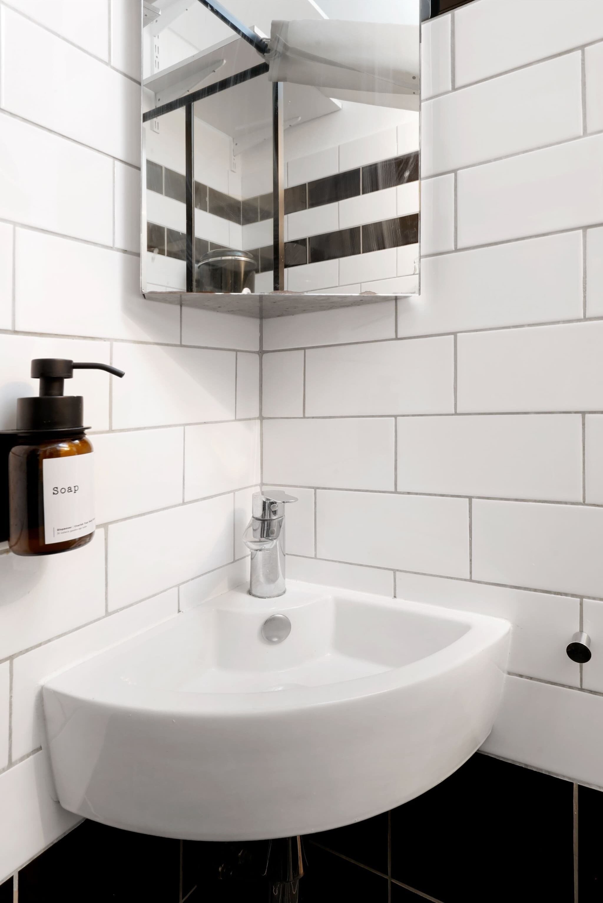 Un baño moderno con un lavamanos blanco, un dispensador de jabón y un espejo.