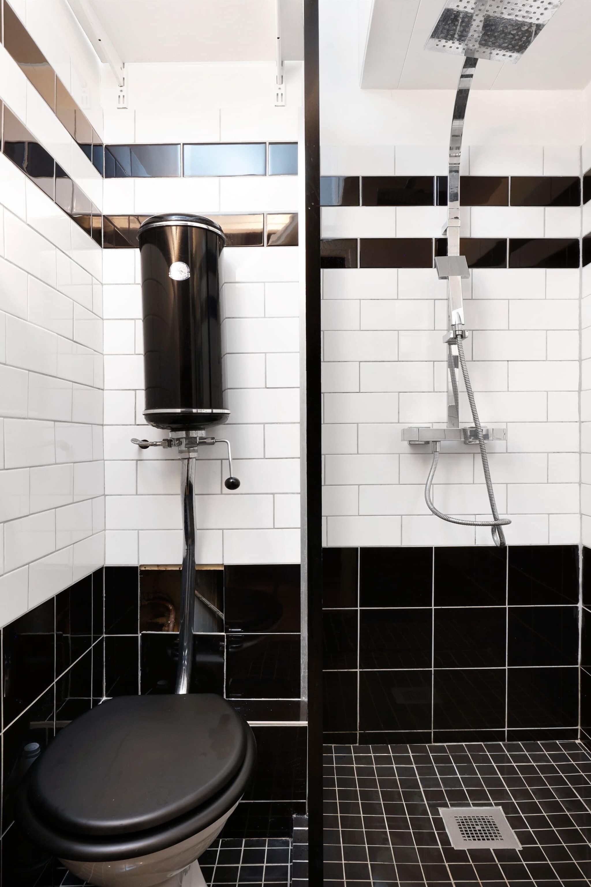 Ein Badezimmer mit Toilette, einer schwarzen Mülltonne und einer Dusche mit einem Chromduschteich.