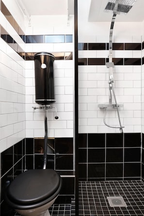 Ein Badezimmer mit Toilette, einer schwarzen Mülltonne und einer Dusche mit einem Chromduschteich.