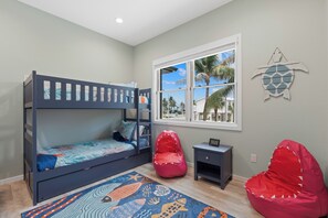 A child's bunk bed with a view of palm trees through the window, a small nightstand, and a red bean bag chair. - 🌴Seaside Cottage | Steps to the Beach 🏖️ Gulf Sunsets & Island Bliss 🌅 (Fort Myers Beach)