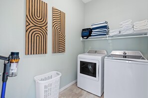 A laundry room with a washing machine, dryer, stacked towels, and a laundry basket. - 🌴Seaside Cottage | Steps to the Beach 🏖️ Gulf Sunsets & Island Bliss 🌅 (Fort Myers Beach)