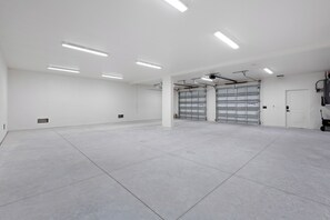 Et rummeligt indendørs område med et rent, hvidt interiør, der inkluderer et stort åbent rum, to garageporte og overflademonteret lys.