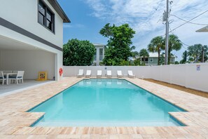A rectangular swimming pool with a tiled deck, surrounded by a white fence, and a covered patio area with white chairs. - 🌴Seaside Cottage | Steps to the Beach 🏖️ Gulf Sunsets & Island Bliss 🌅 (Fort Myers Beach)
