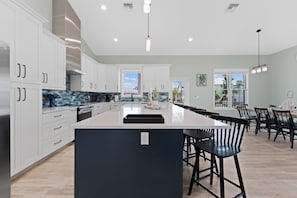A modern kitchen with white cabinets, a large island, and a dining area with bar stools. - 🌴Seaside Cottage | Steps to the Beach 🏖️ Gulf Sunsets & Island Bliss 🌅 (Fort Myers Beach)