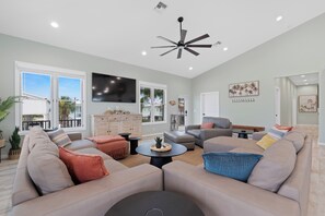 Un salon spacieux avec un grand canapé d’angle, un téléviseur à écran plat et un ventilateur de plafond.