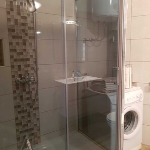 Ein Badezimmer mit einer Dusche in Glasabtrennung, einem Waschbecken und einer Waschmaschine.
