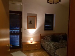 Ein Schlafzimmer mit einem Bett, einem Nachttisch mit Lampe, einem gerahmten Bild an der Wand und einem Fenster mit Jalousien.