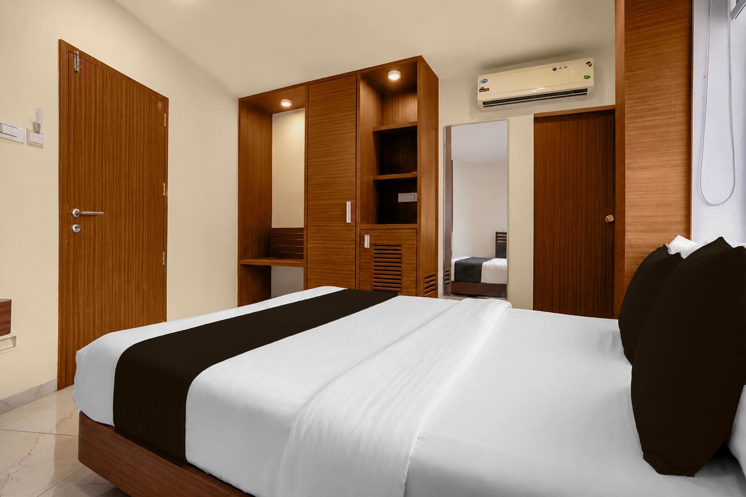 A hotel room with a bed, wooden wardrobe, and an air conditioning unit.
