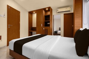 A hotel room with a bed, wooden wardrobe, and an air conditioning unit.