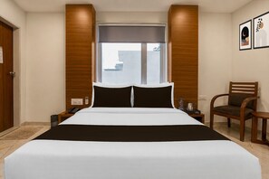 A hotel room with a large bed, a window with a view, a wooden headboard, a chair, and a small table.