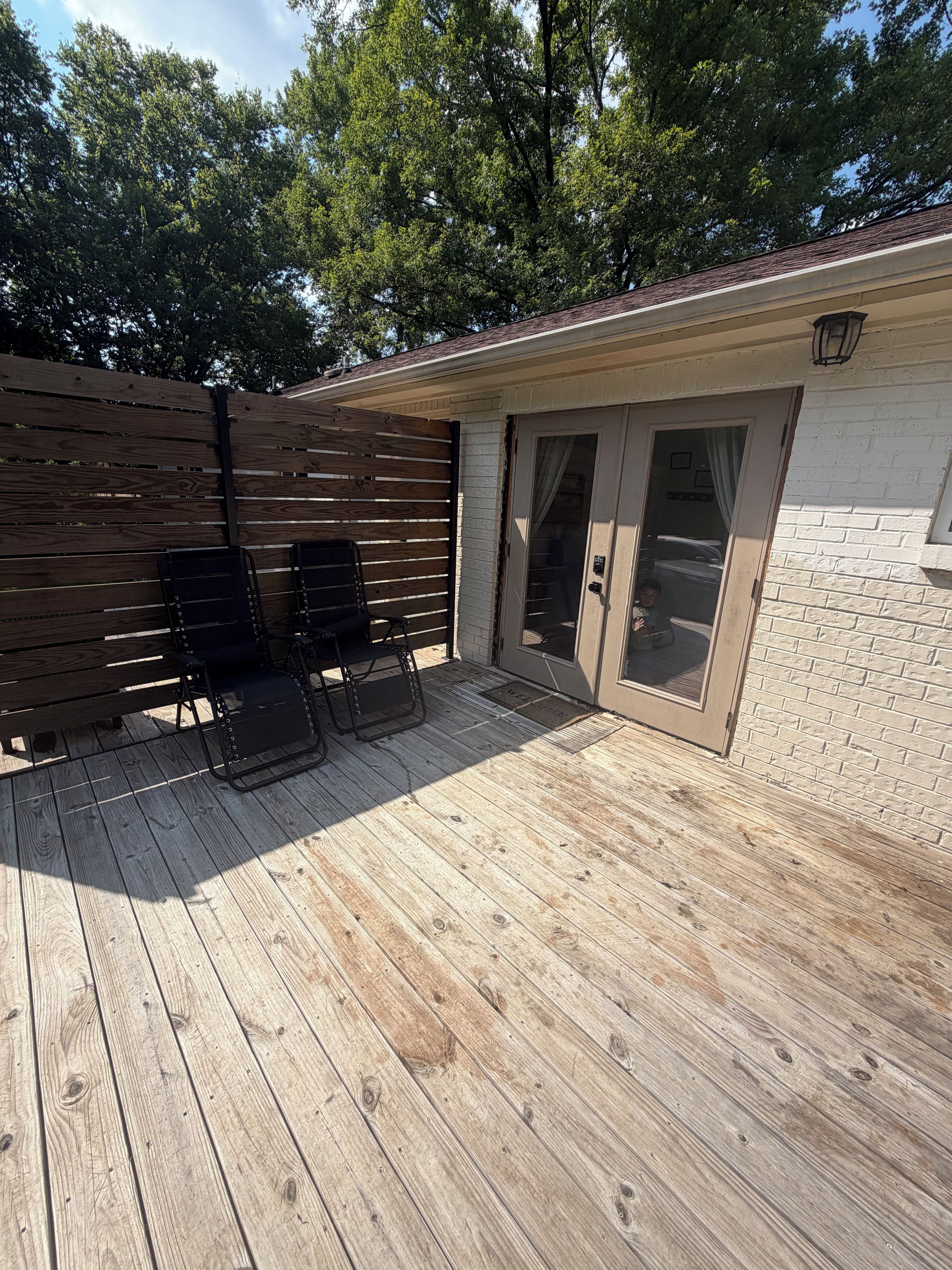A wooden deck with two black chairs and a door leading to a covered area.