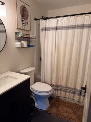 Een badkamer met een wit toilet, een zwart wastafelmeubel, een douchegordijn en een bruine badmat.