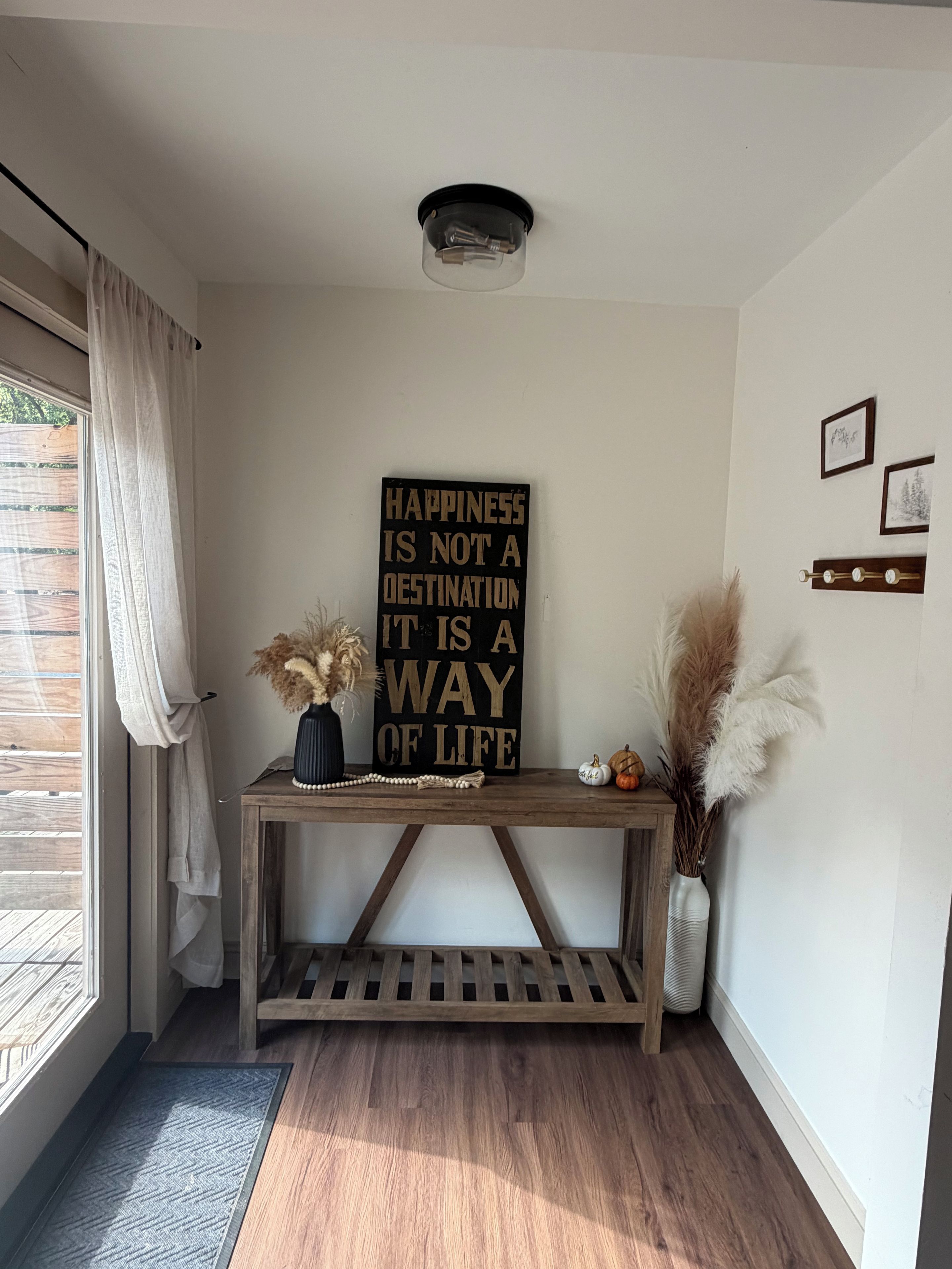A room with a wooden console table, a sign with a motivational quote, and decorative plants.