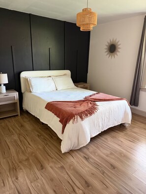 A bedroom with a bed, a nightstand, a hanging light fixture, and a wall decoration.