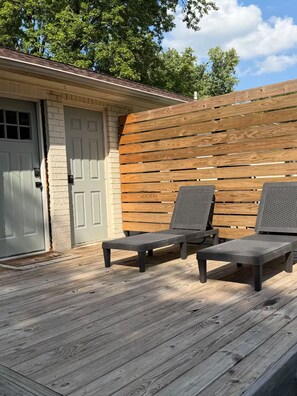 Een terras met twee ligstoelen en een houten wand.
