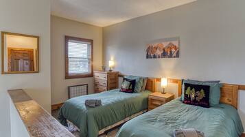 A room with two beds, a wooden bench, a window with blinds, a radiator, and a wall-mounted painting.