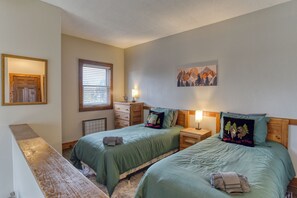 Een kamer met twee bedden, een houten bankje, een raam met zonwering, een radiator en een schilderij aan de muur.