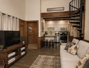 A living room with a television, a sofa, and a kitchen in the background.