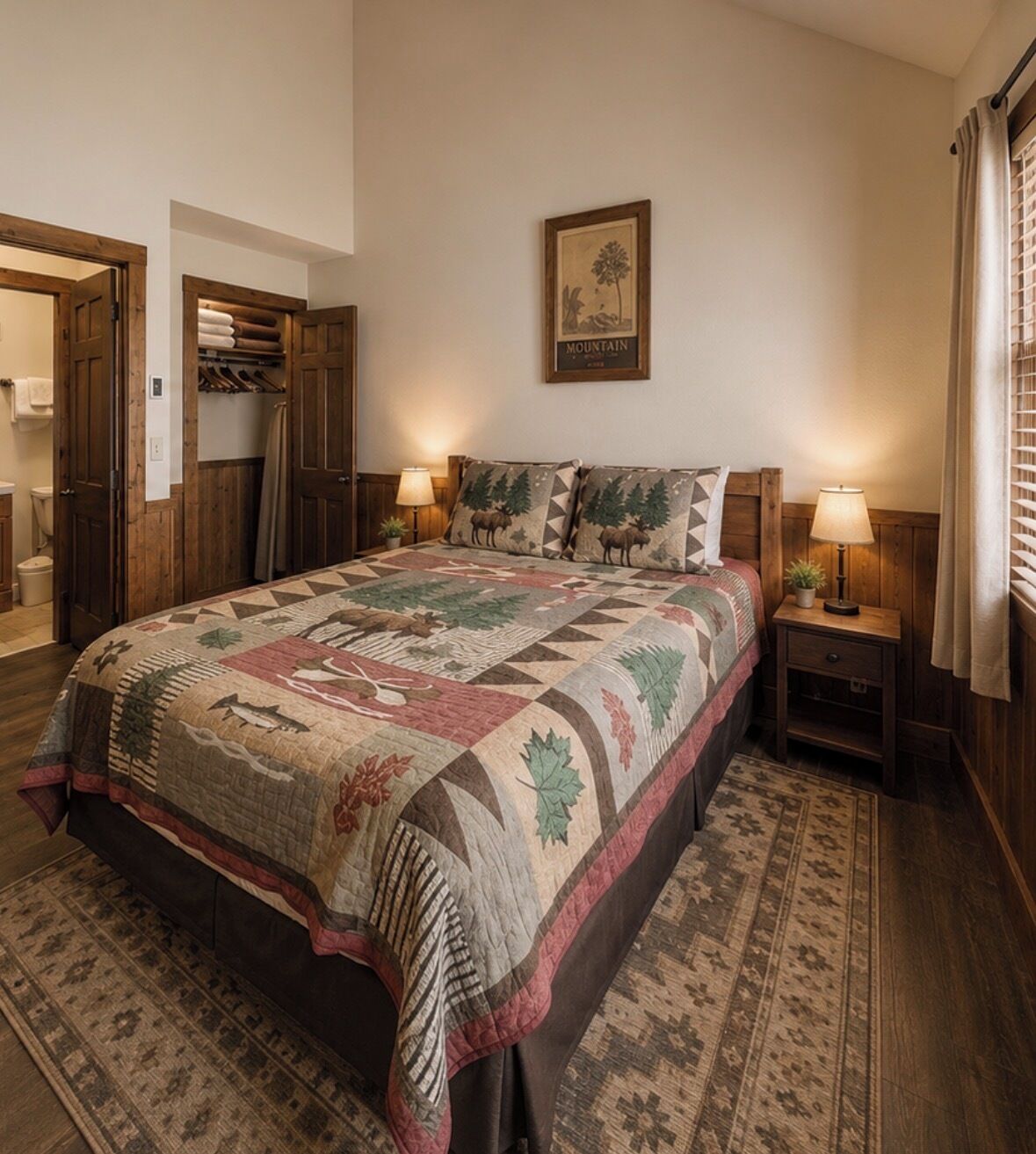 A bedroom with a large bed, wooden headboard, two bedside tables with lamps, a framed picture on the wall, and a patterned rug.