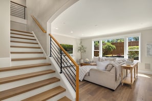 A modern interior with a wooden staircase, a living area with a sofa and coffee table, and a large window offering a view of the outdoors. - Luxury Family Home Minutes from Downtown Kirkland (Kirkland)