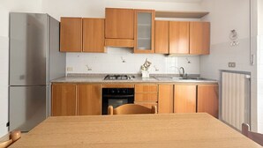 A compact kitchen with wooden cabinets, a stainless steel refrigerator, a gas stove, and a sink. - A50 - Massignano, spacious four-room apartment (Massignano)