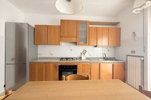 Eine kleine Küche mit Holzschränken, einem Edelstahlkühlschrank, einem Gasherd und einem Spülbecken.
