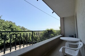 Ein Balkon mit weißem Tisch und Stühlen, einem Metallgeländer und Blick auf Grünflächen.
