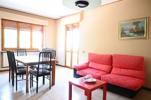 Ein Zimmer mit Esstisch, Stühlen, einem roten Sofa und einem Gemälde an der Wand.