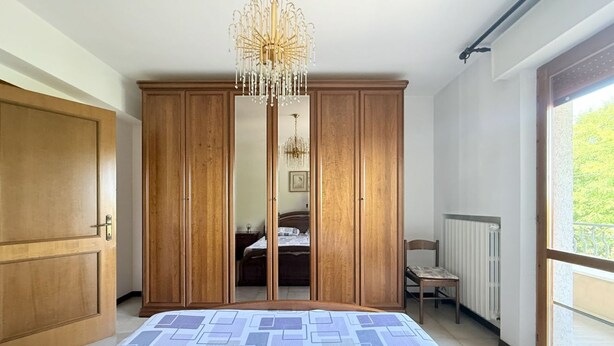 A bedroom with a large bed, wooden wardrobe, and a chandelier. - A50 - Massignano, spacious four-room apartment (Massignano)