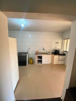 A kitchen with white tiles, a gas stove, a sink, and a window. - Barreirinhas Village (Barreirinhas)