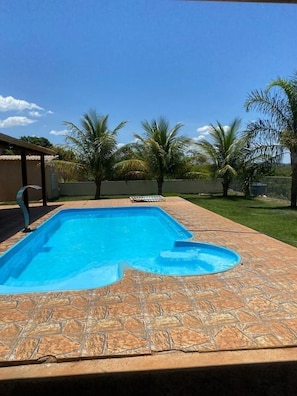 A rectangular swimming pool with a stone tile deck, surrounded by a grassy area and palm trees. - Barreirinhas Village (Barreirinhas)