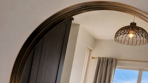 A room with a large mirror, a chair, a small table, and a view of the sea through a window.
