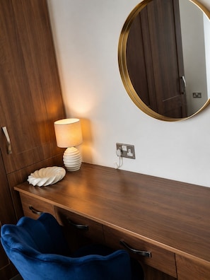 Een houten wastafelmeubel met een ronde spiegel, een lamp en een decoratief object op het aanrecht.