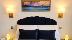 A hotel room with a large bed, two bedside lamps, a painting above the bed, and a nightstand with a lamp.