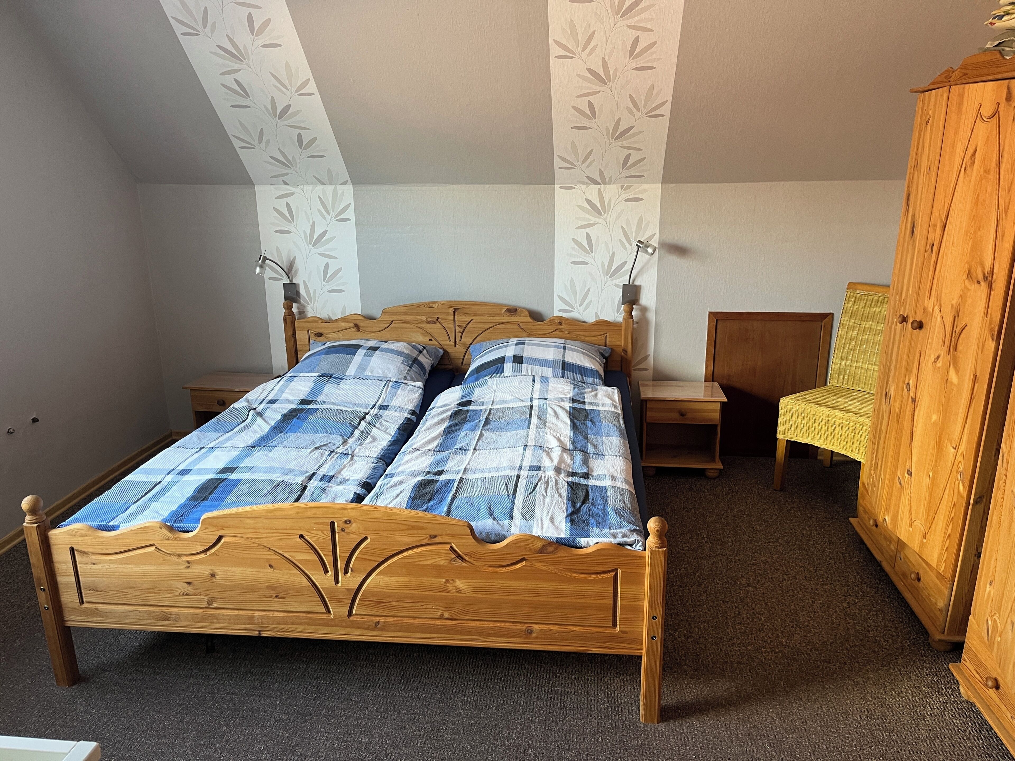 A bedroom with a wooden bed, two bedside tables, a chair, and a wardrobe.