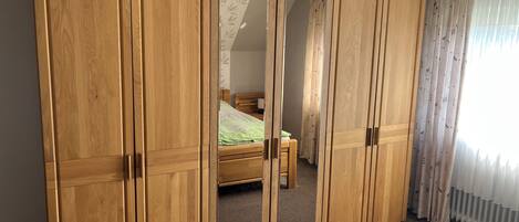 A room with a large wooden wardrobe, a bed with green bedding, and a window with sheer curtains.