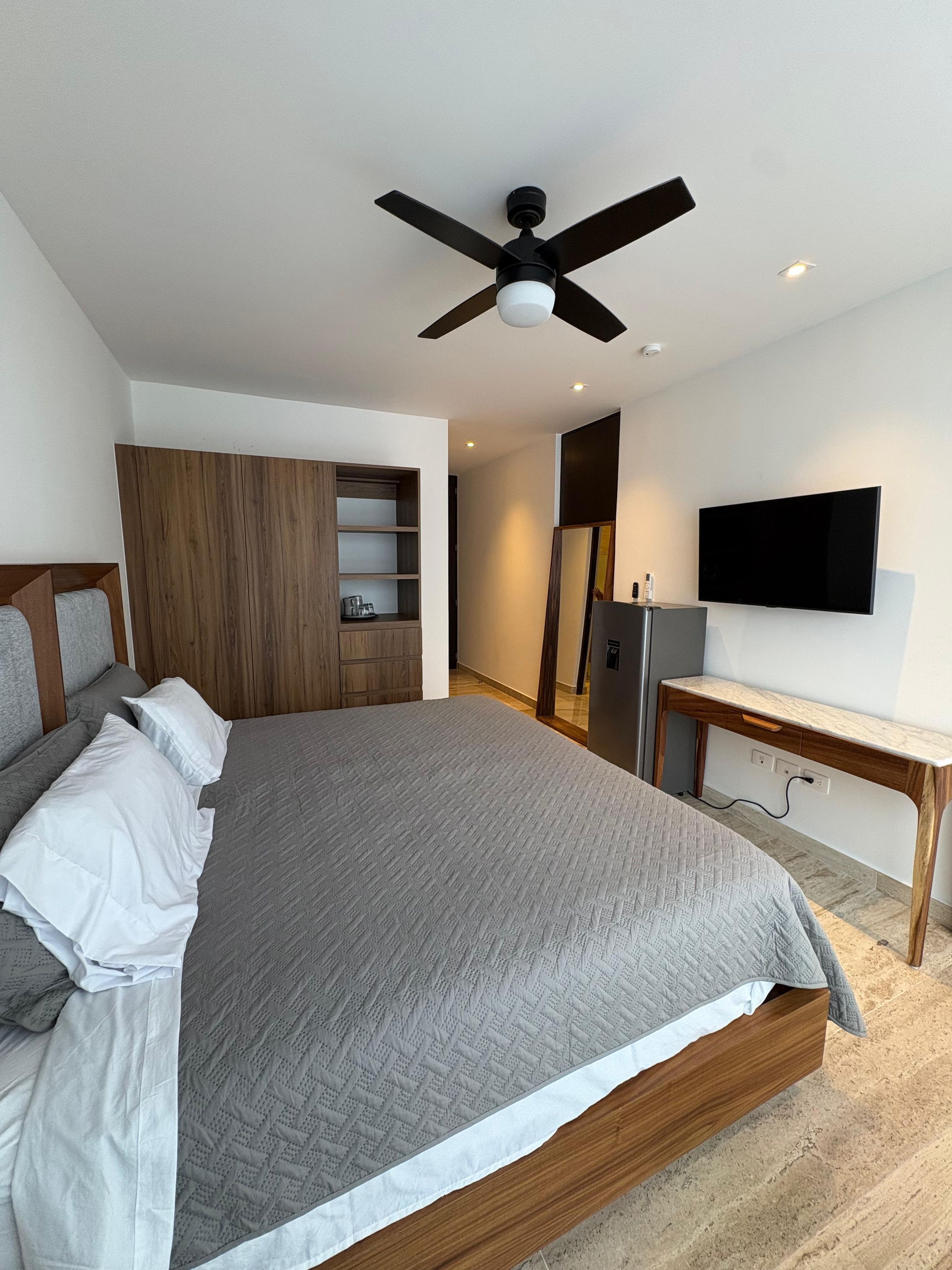 Un dormitorio moderno con una cama grande, un ventilador de techo, un televisor y un armario de madera.