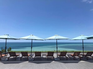 Une terrasse avec des chaises longues et des parasols, donnant sur une mer d’un bleu limpide.