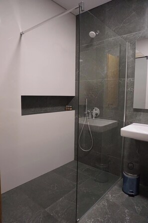 Ein modernes Badezimmer mit einer gläsernen Duschkabine, einem integrierten Waschbecken und einem Mülleimer.