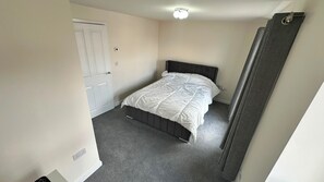 A small, single-bed room with a grey carpet, a white door, and a dark headboard. - Sheffield Charm - Cozy 2 Bedroom House (Sheffield)