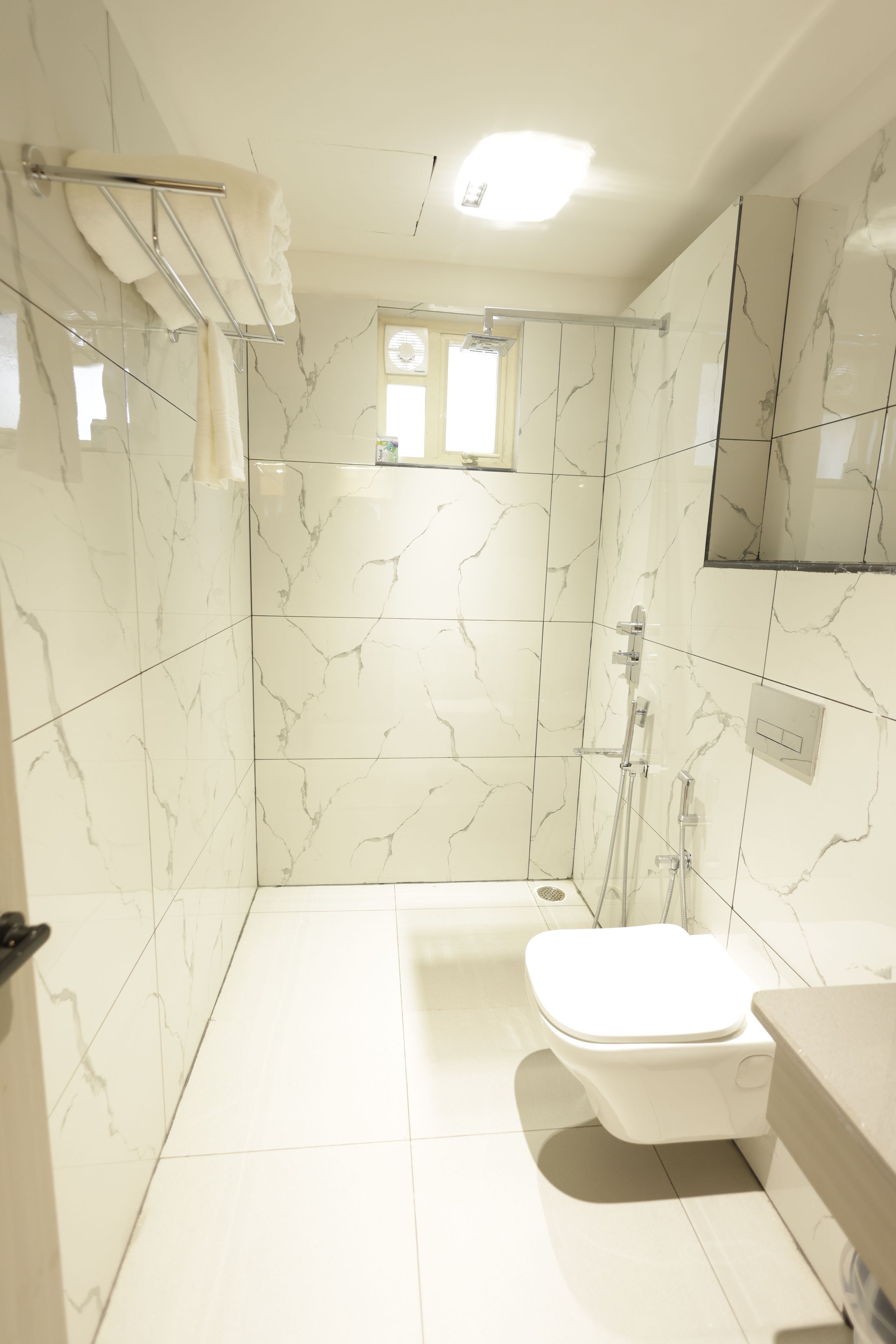 Une salle de bain avec des carreaux de marbre blanc, des toilettes, un espace douche et un miroir.