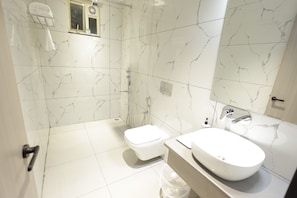 Un baño con inodoro blanco, lavamanos y zona de ducha.