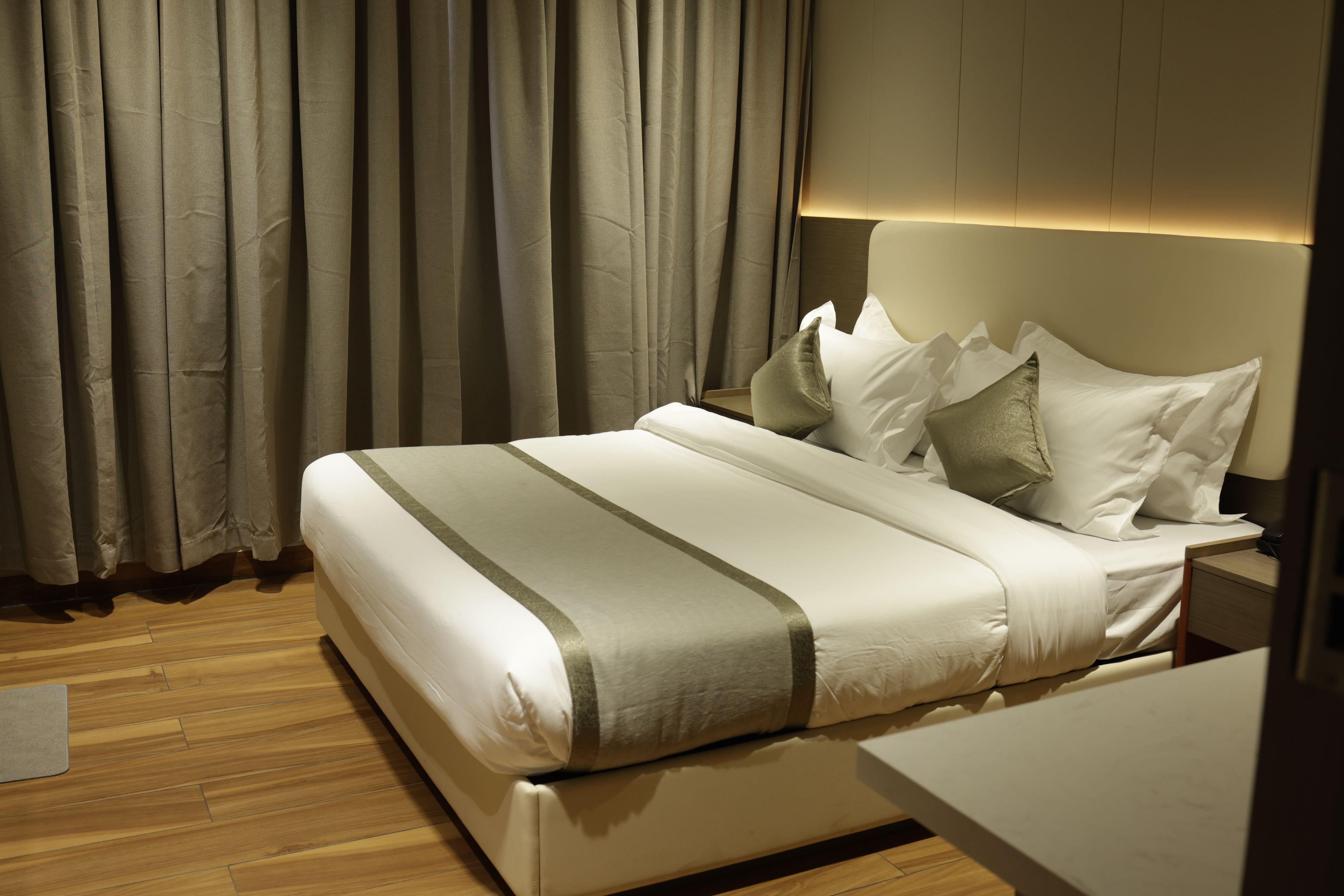 Habitación de hotel moderna con una cama grande, piso de madera y vista al cielo nocturno a través de cortinas.
