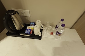 Bandeja de desayuno en una habitación de hotel, con cafetera, bolsitas de té, sobres de azúcar, taza y botellas de agua.