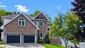 Une maison à deux étages avec une façade en briques, deux portes de garage et une pelouse bien entretenue.