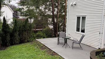 Il s’agit d’une propriété résidentielle dotée d’une terrasse, d’une petite table et de chaises, ainsi que d’un jardin avec de la pelouse et des arbres.