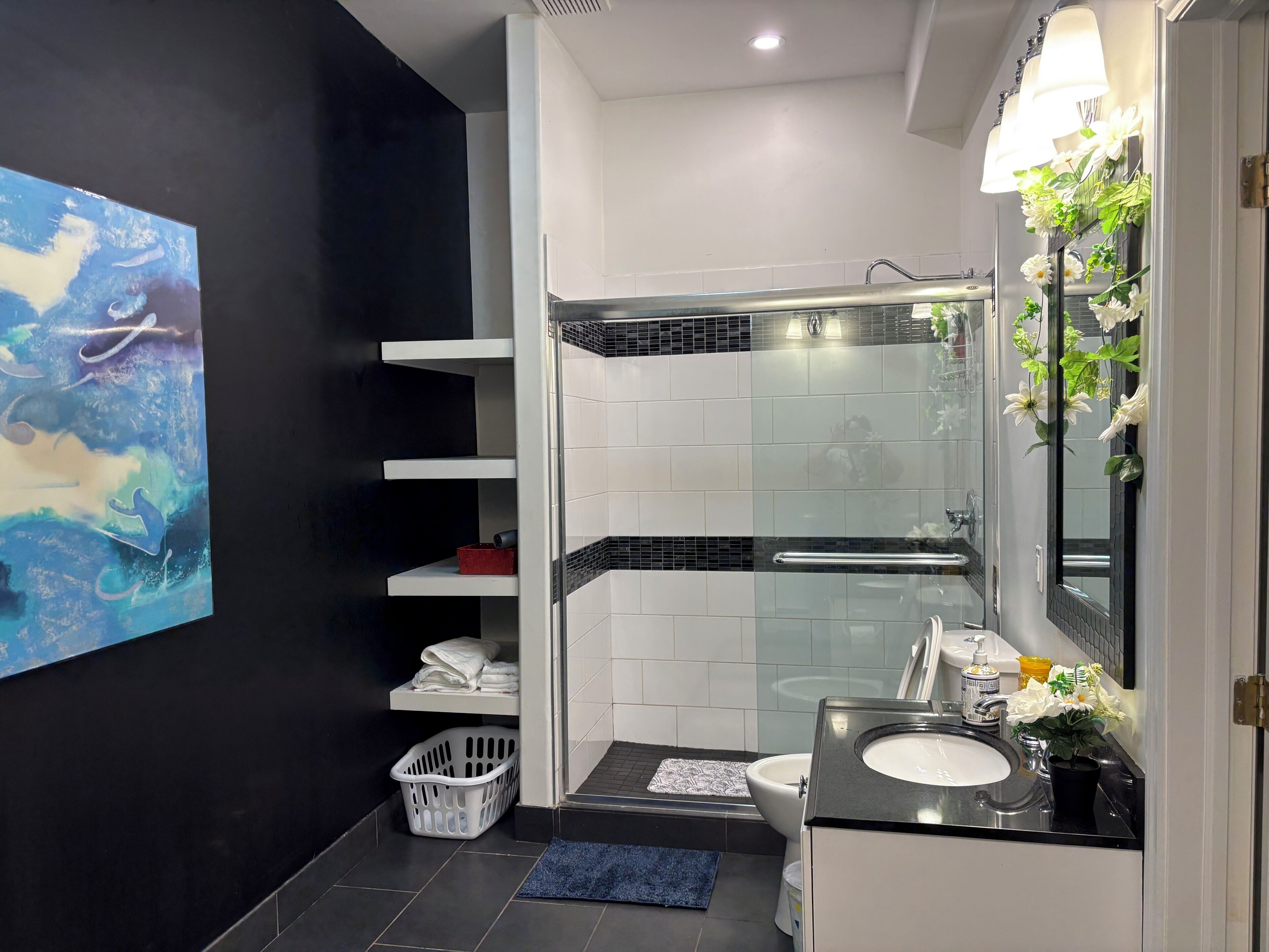 Une salle de bain moderne avec une douche à l’italienne en verre, un lavabo blanc et un grand miroir orné de motifs floraux.