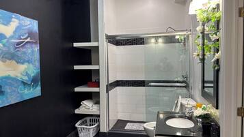 Une salle de bain moderne avec une douche à l’italienne en verre, un lavabo blanc et un grand miroir orné de motifs floraux.
