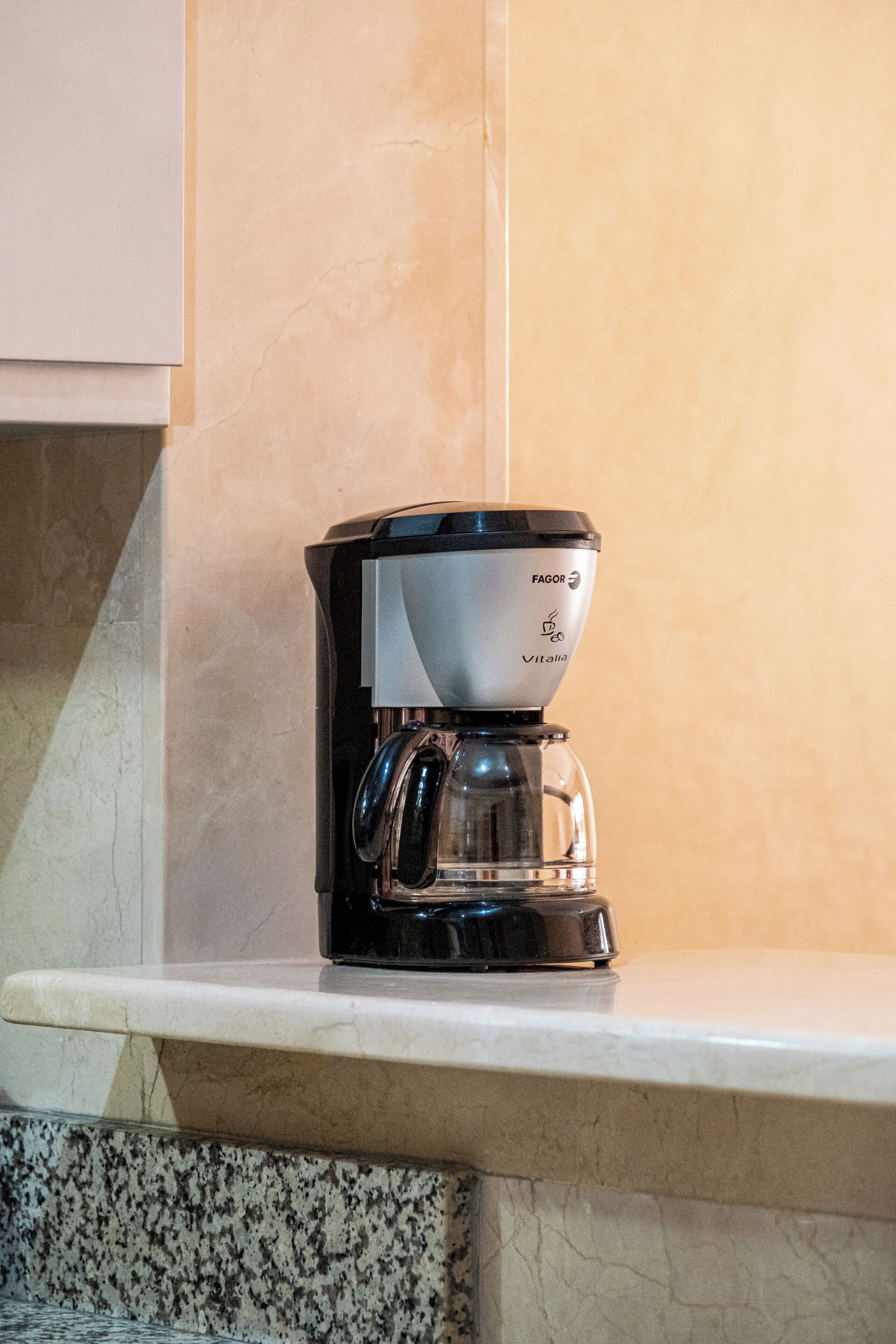 Une machine à café posée sur un plan de travail de cuisine, avec un pare-éclaboussures en marbre.